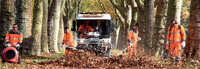 4 Mitarbeitende der AWB Straßenreinigung und eine Kehrmaschine beseitingen mit Besen und Gerät Laub. 